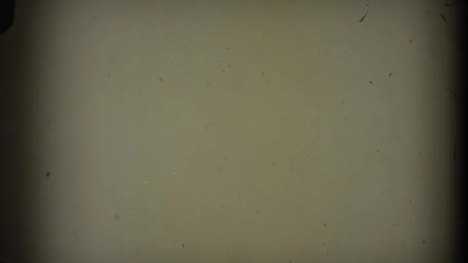 A pale, mostly blank 8mm frame shows soft exposure, dust, small scratches, and a dark edge from the film gate.