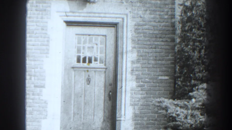 Cumberland, Maryland doorway detail from 1938 home-movie footage, with a closed wooden door, divided window, brickwork, and shrubbery.