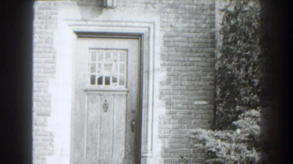 Final 1938 Cumberland doorway frame showing the closed wood door, grid window, light trim, brick wall, shrub, and dark 8mm vignette.
