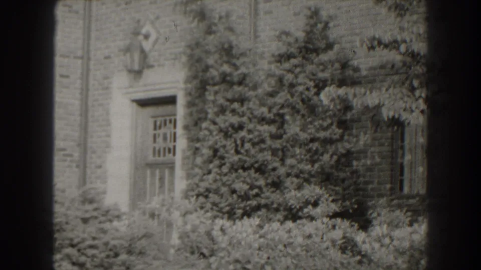 1938 Cumberland, Maryland home-movie frame of a brick entrance and overgrown landscaping, partly framed by the film edge.
