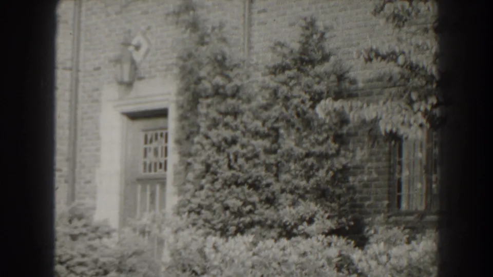 1938 Cumberland, Maryland exterior frame with a wooden door at left, dense plantings and a window set into the brick wall.