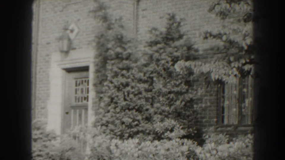 1938 Cumberland, Maryland frame of a still exterior facade with door, lantern, leafy landscaping and a window at the right.