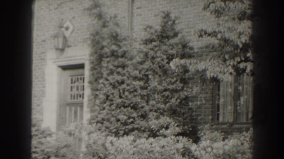 1938 Cumberland, Maryland home-movie frame showing a brick house doorway and windows partly obscured by dense foliage.