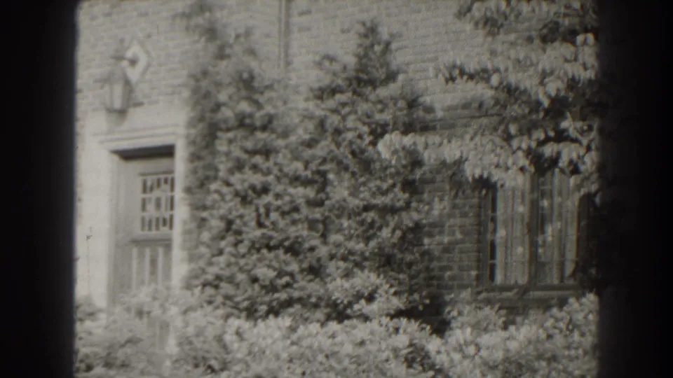 1938 Cumberland, Maryland view of a brick residential exterior, with windows and a doorway partly covered by trees and shrubs.