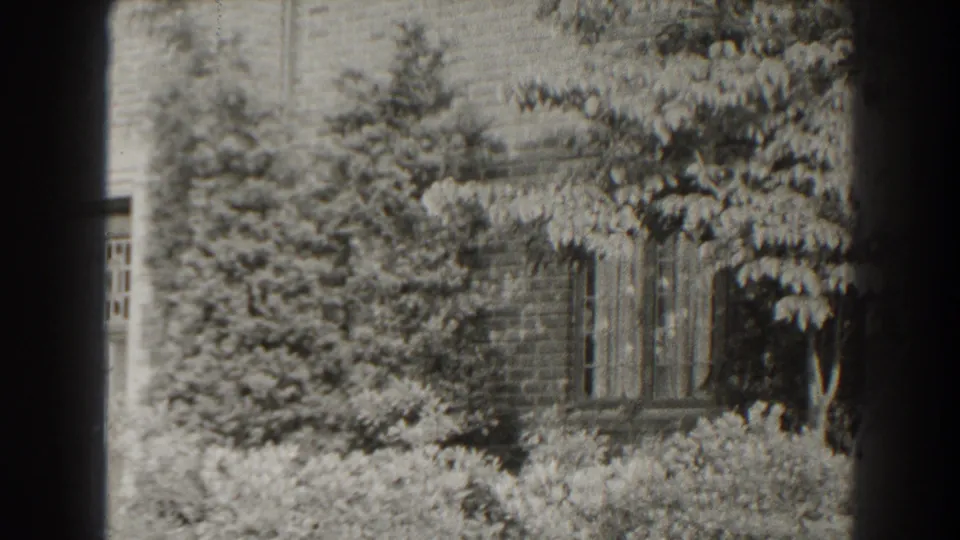 1938 Cumberland, Maryland home-movie frame showing a brick house facade and windows largely screened by trees and shrubs.