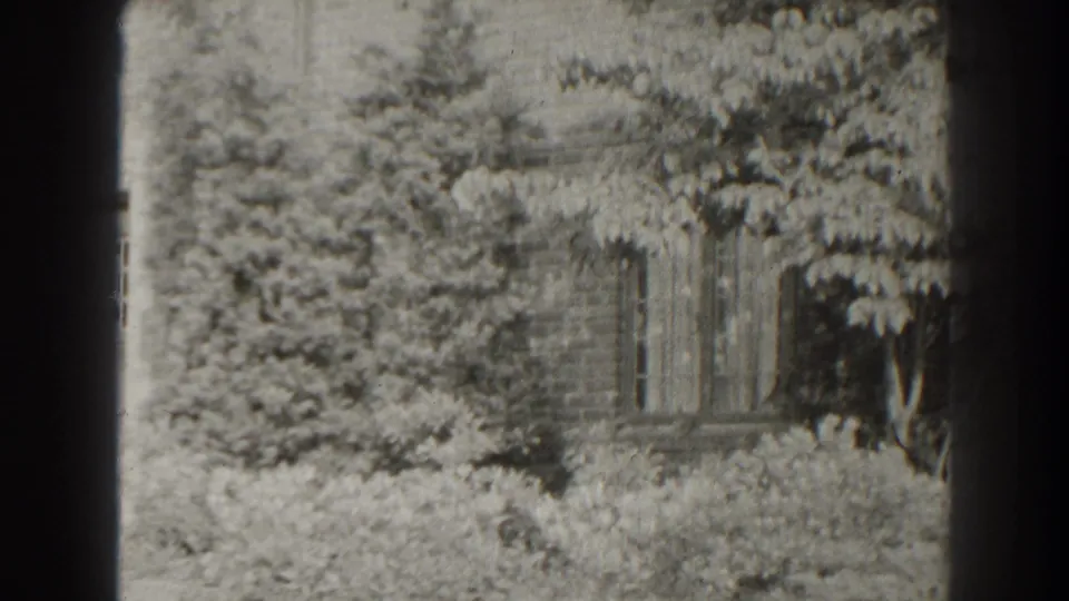 1938 Cumberland, Maryland 8mm frame showing shrubs, trees, a building wall, and a glimpse of old stone garden structure.