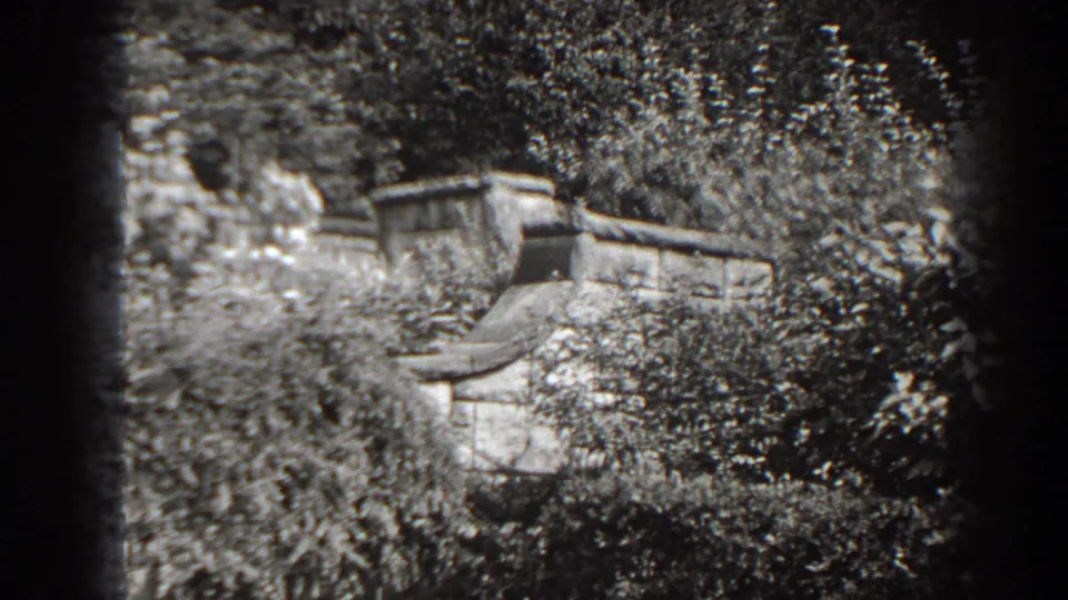Cumberland, Maryland 1938 8mm frame showing an old masonry wall framed by dark shrubs, trees, and soft black-and-white film texture.