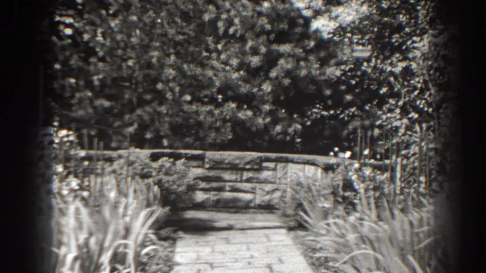 1938 black-and-white home-movie frame showing a planted garden walkway and low stone wall in Cumberland, Maryland.