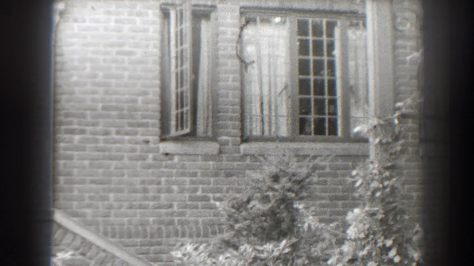Cumberland, Maryland 1938 frame showing a brick facade, tall multi-pane windows, shrubs, and a lantern-style fixture.