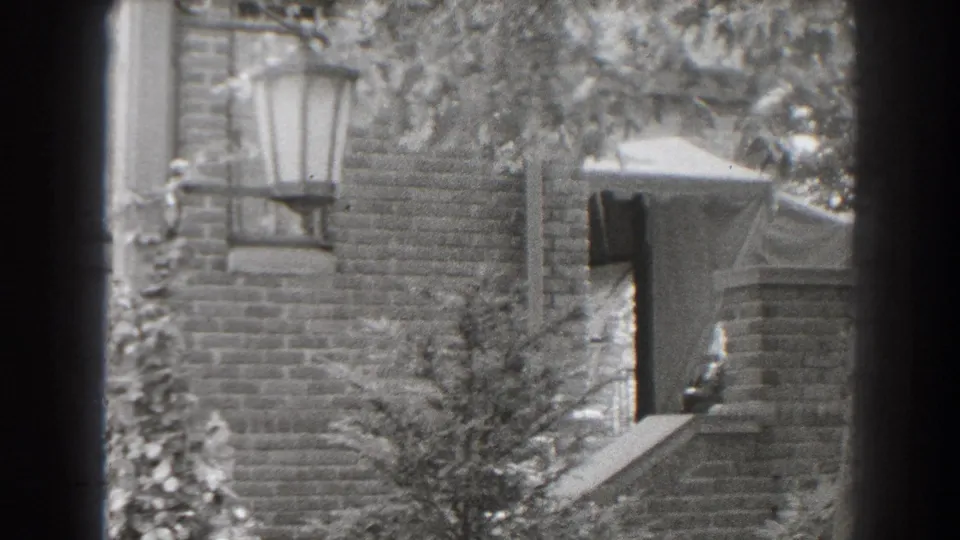 1938 Cumberland, Maryland home-movie frame showing a brick house entrance with awning, lantern-style light, steps, and foliage.