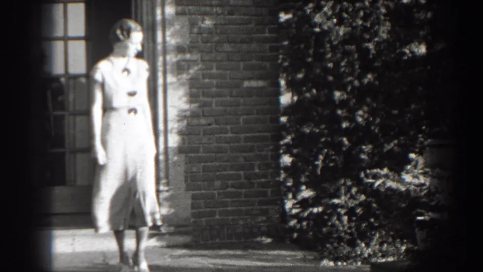 Adult woman in 1938 Cumberland, Maryland stands by steps and a brick doorway in black-and-white 8mm footage.