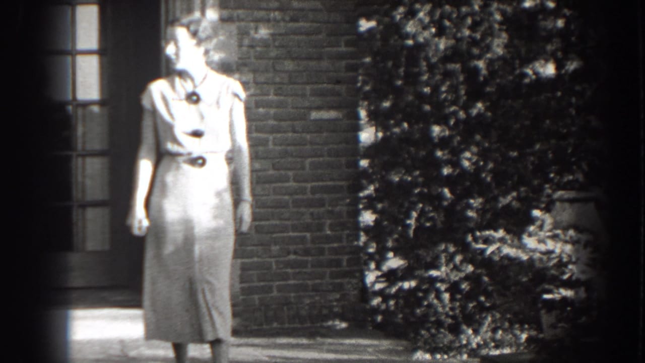 Woman in a light dress looks to the side beside a brick wall and shrubs.
