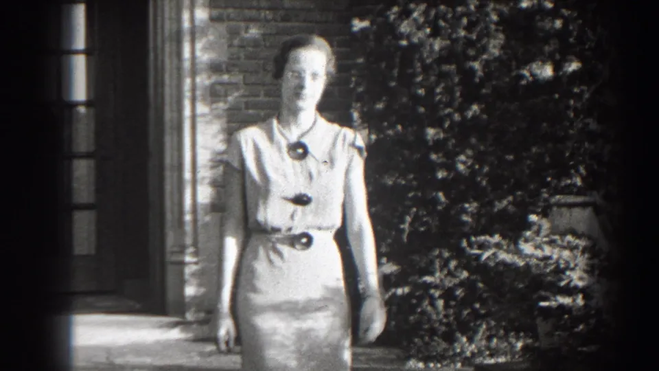 Adult woman faces the camera outside a brick building in 1938 Cumberland, Maryland home-movie footage.