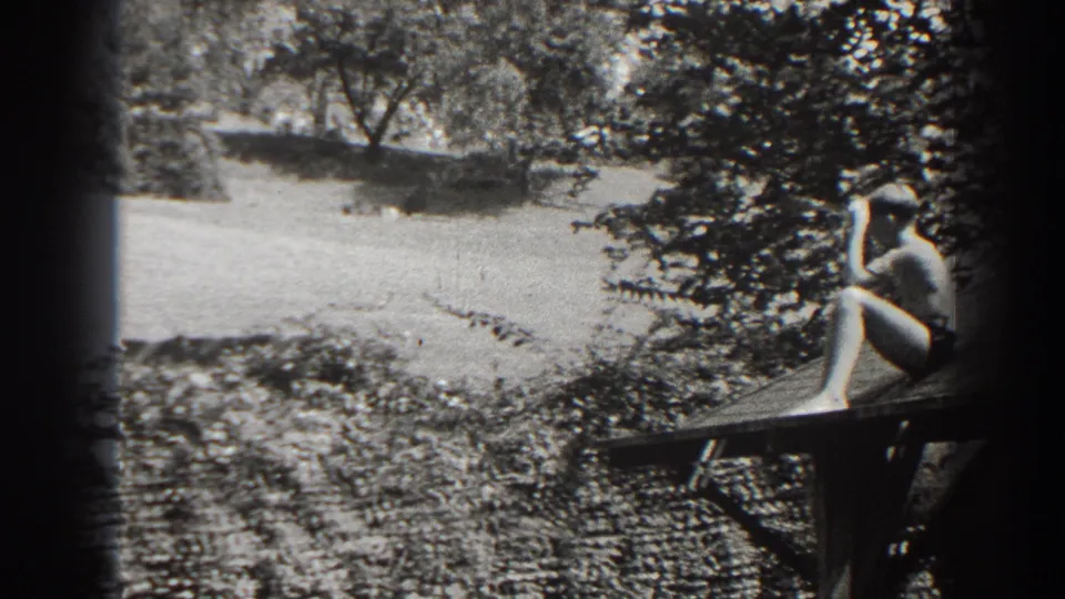 In 1938 Cumberland, Maryland home-movie footage, a boy sits on a wooden platform overlooking a sunlit grassy hill with trees.