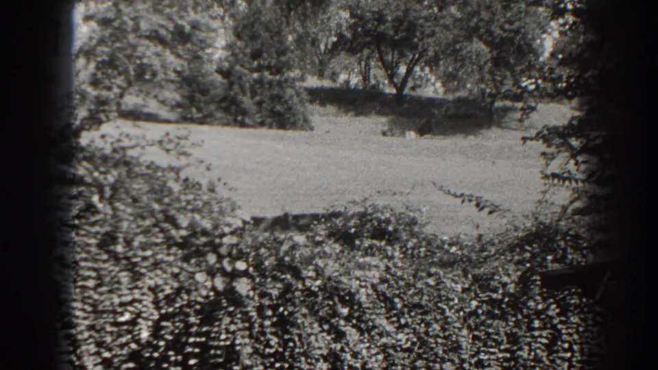 A black-and-white 8mm frame shows the grassy Cumberland hillside, surrounding trees, low shrubs, and a platform edge during the pan.