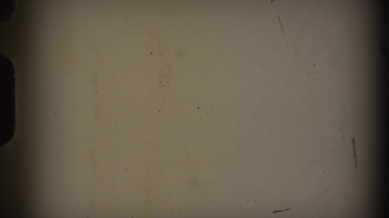Pale blank film frame with dust, scratches, and dark edge vignetting.
