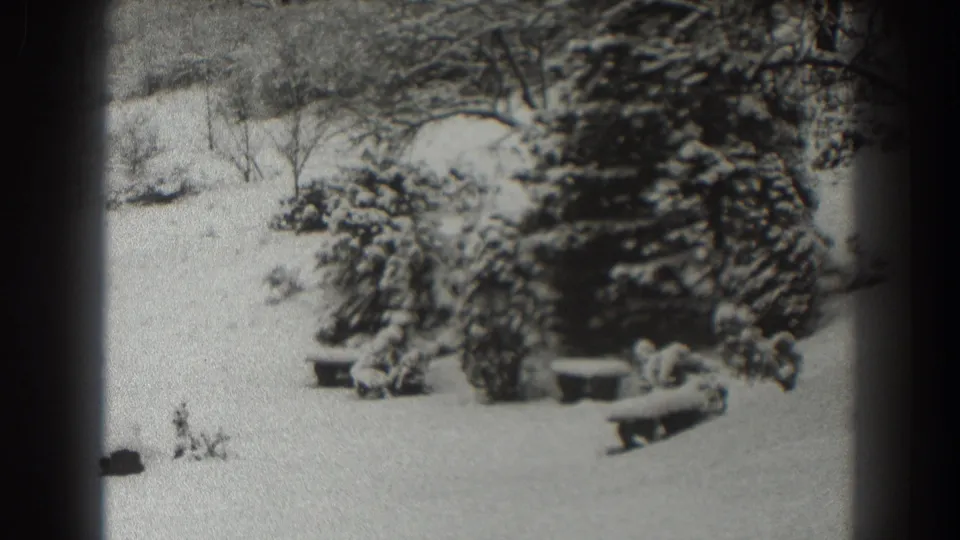 Snow-covered pines and garden benches appear in a Martinsburg winter yard, framed by soft black-and-white 8mm film edges.