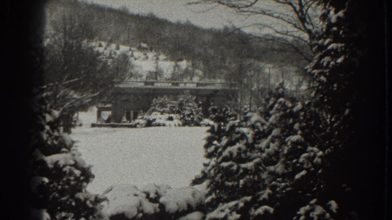 Snow-covered house and hillside framed by trees in a black-and-white winter view.