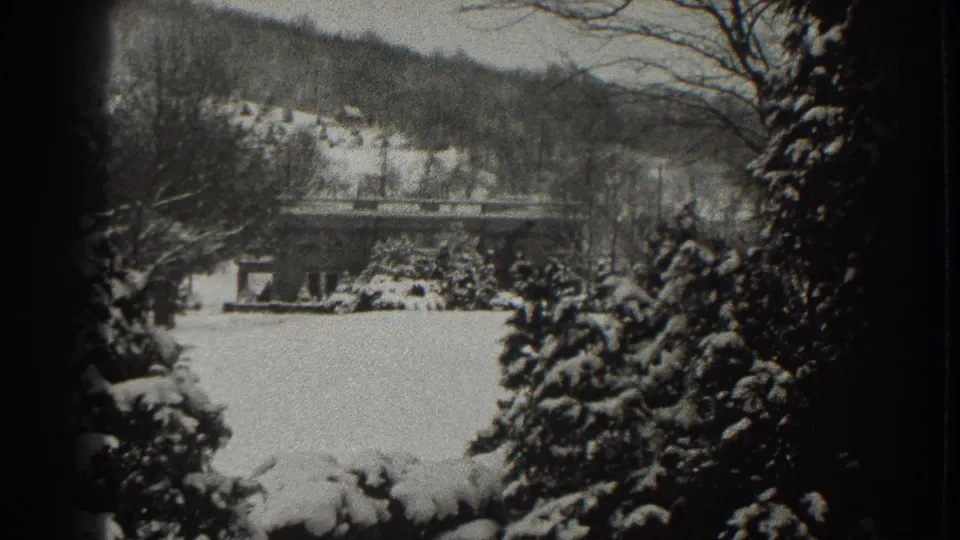 1938 Martinsburg, West Virginia winter view with a small snow-covered house, hillside, bare trees, and dark 8mm frame edges.