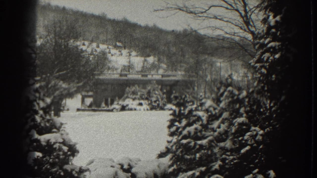Snowy hillside scene with a low house, trees, and a bridge or raised roadway.