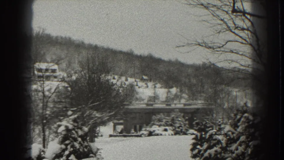 Late-1930s 8mm frame from Martinsburg showing a snow-covered landscape, low bridge, bare trees, and hillside houses.