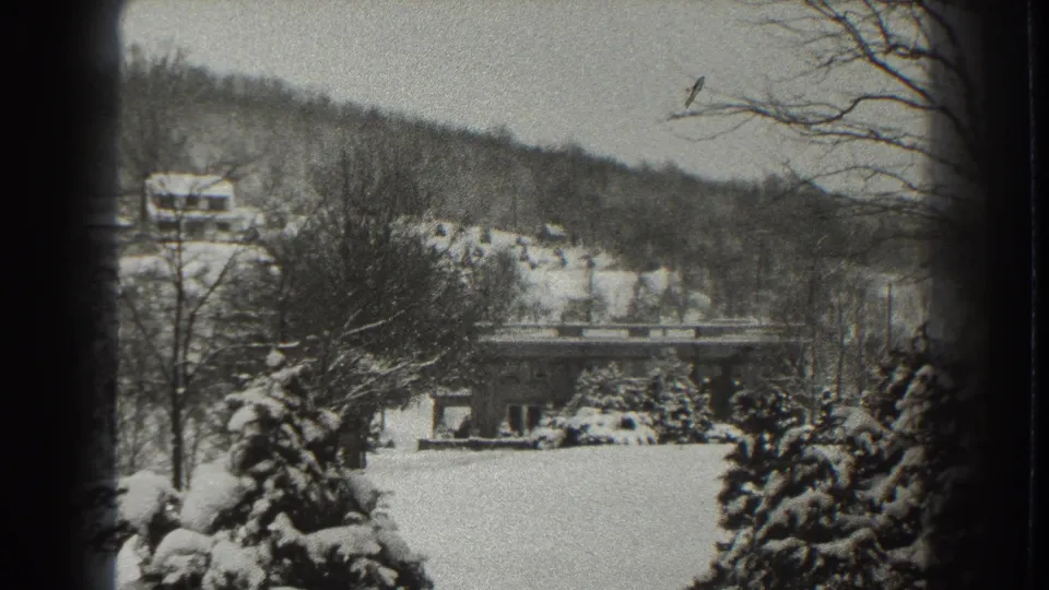 Snowy Martinsburg winter scene from 1938, showing evergreens, bare trees, a distant building, and hills within visible 8mm frame edges.