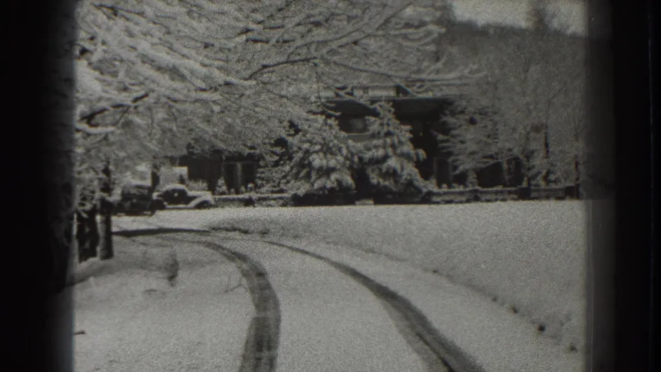 1938 Martinsburg winter road scene with tire tracks curving through snow toward trees and distant buildings in black-and-white home-movie footage.
