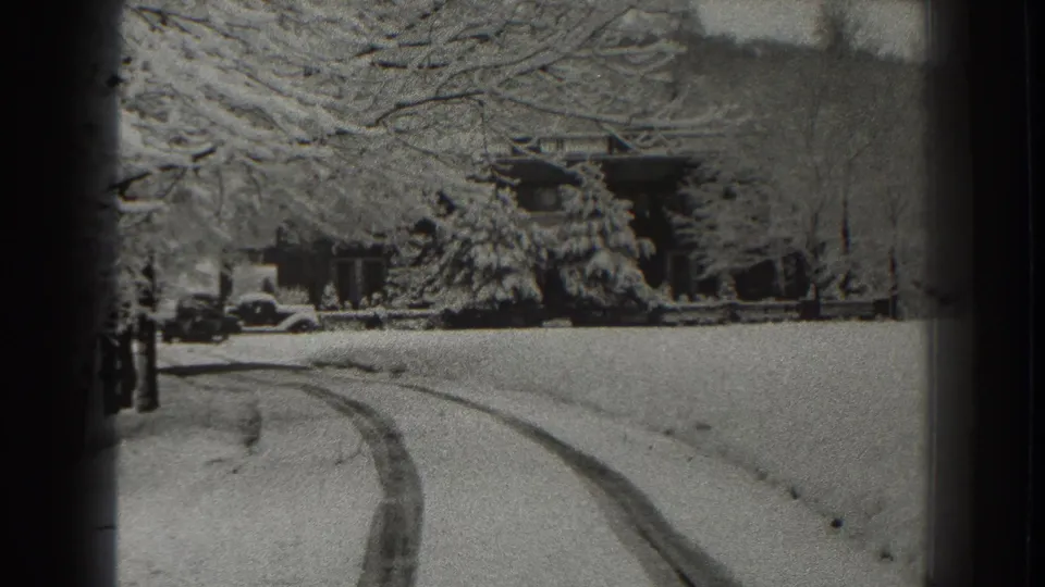 Snowy road in Martinsburg, West Virginia, 1938, with tire tracks, winter trees, and distant buildings seen through soft black-and-white 8mm texture.