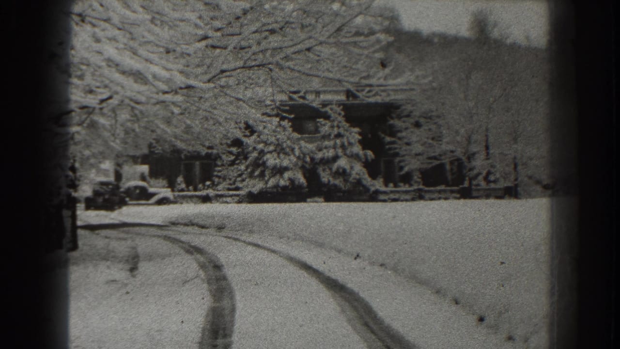 Snowy rural road with tire tracks leading toward a house and parked car.