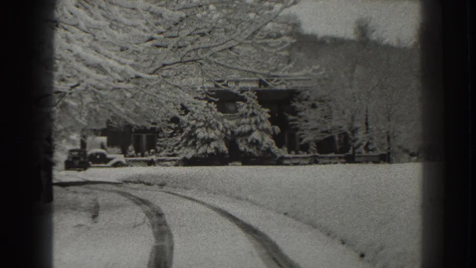 Fixed 8mm view in Martinsburg, West Virginia, with snow-covered tire tracks, a house, winter trees, and an automobile near the property.