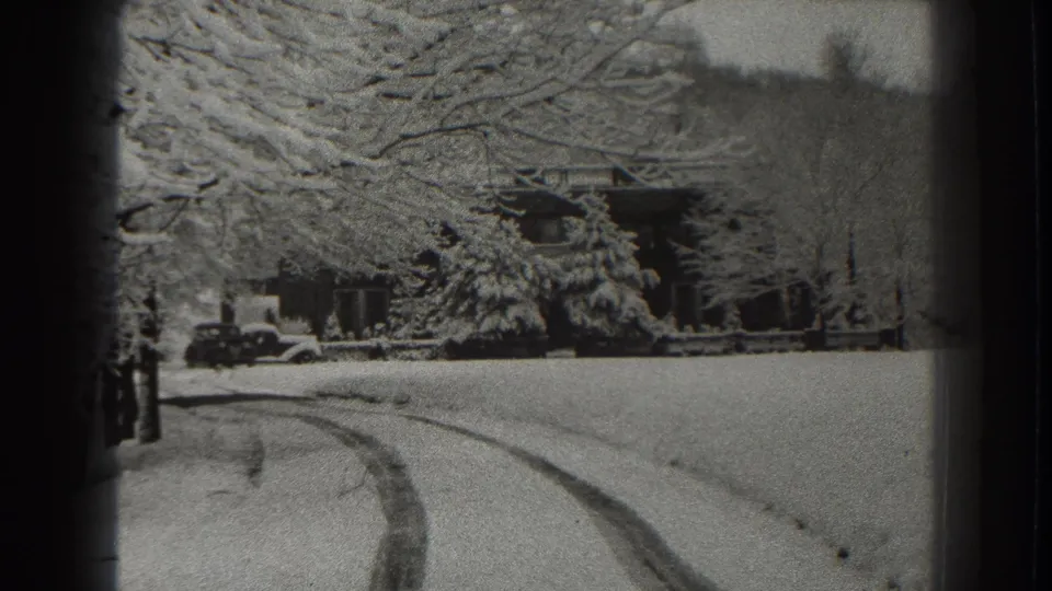 Black-and-white 1938 home-movie frame of a Martinsburg winter scene with tire tracks, a distant house, trees, and a parked car.