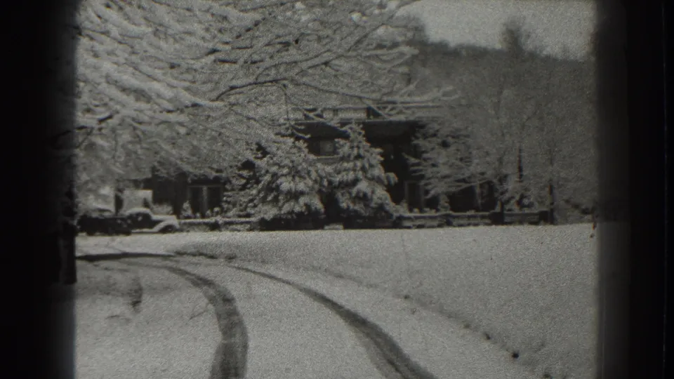 1938 Martinsburg-area 8mm frame showing tire tracks through snow leading toward a lodge or cabin under snow-laden trees.