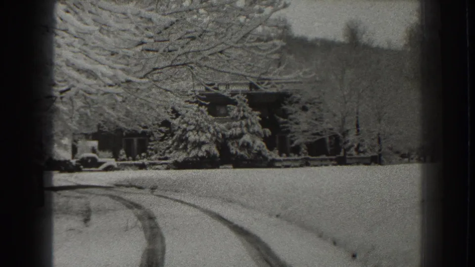1938 Martinsburg-area home-movie view of a snowy drive, parked car, and lodge-like building beneath heavy winter branches.