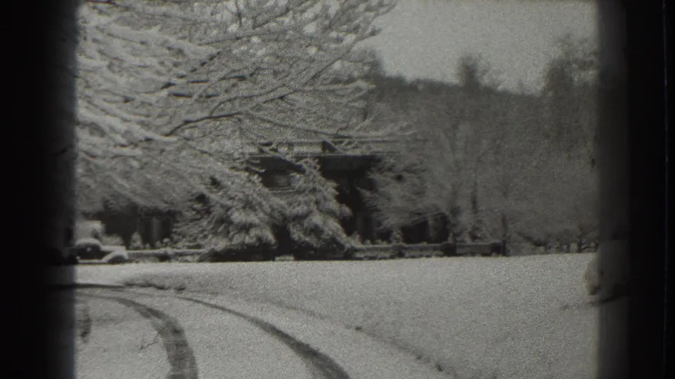 1938 Martinsburg-area 8mm frame with a snow-covered foreground, curved track, and lodge or cabin partly obscured by trees.