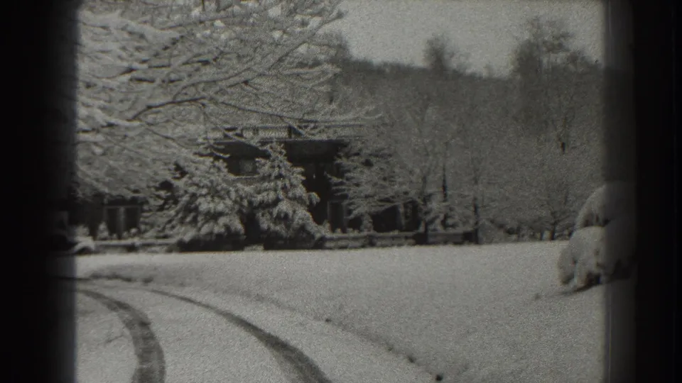 1938 Martinsburg-area winter frame showing tire tracks crossing snow toward a secluded lodge or cabin near a wooded hillside.