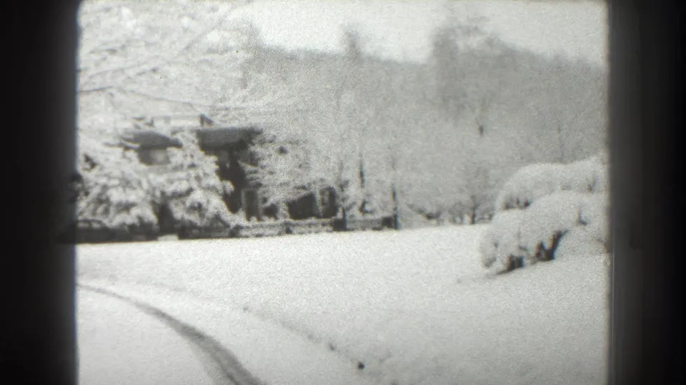 Overexposed 1938 Martinsburg home-movie frame of a snowy rural yard with cabin, bare trees, shrubs, and curved road tracks.