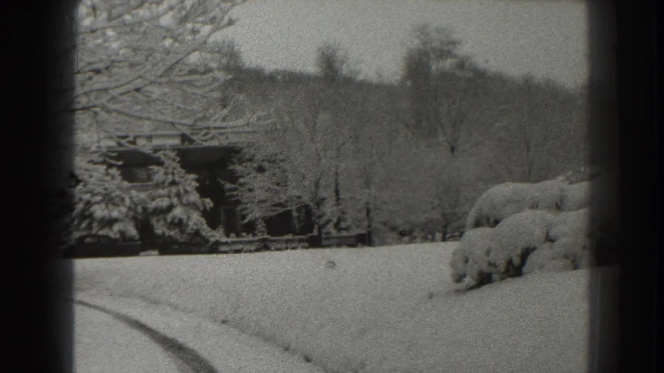 1938 Martinsburg winter frame showing a snow-covered rural landscape with cabin, bare trees, rounded shrubs, hillside, and curved road mark.