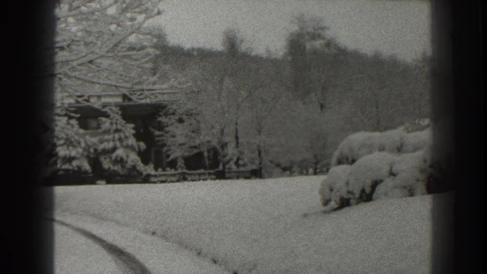 1938 Martinsburg home-movie frame showing a snowy yard, bare trees, heavy shrubs, and a distant residential structure.