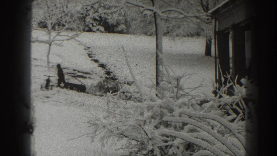 A distant figure walks across a snow-covered yard in Martinsburg, with footprints or a narrow path leading uphill near a building edge.