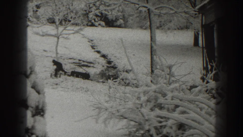 In 1938 Martinsburg, West Virginia footage, a man stands by wood in a snow-covered yard framed by trees and a nearby house.