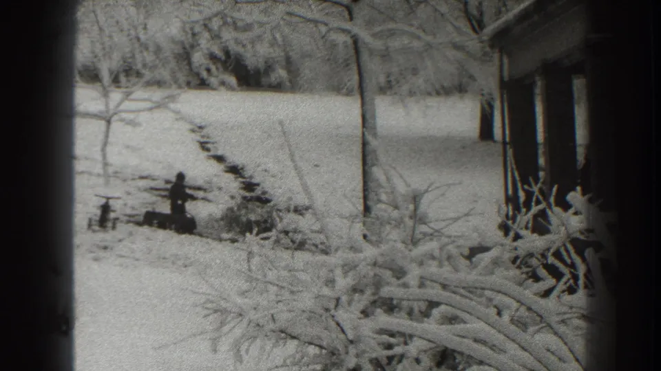The final frame keeps the man small in the snowy Martinsburg yard, with wood, a path, bare trees, and the side of a house in view.