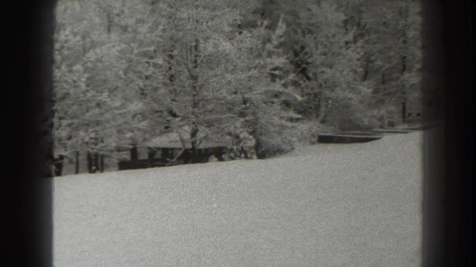 1938 Martinsburg home-movie frame showing a snowy sloping field below bare winter trees and dark film borders.