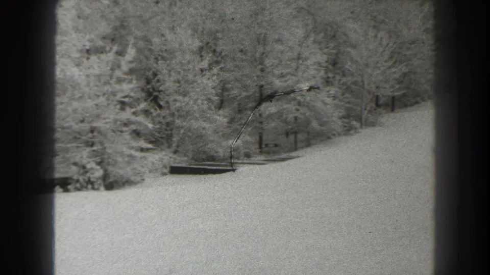 1938 8mm frame of a snow-covered Martinsburg hillside with bare woods and a low dark object at midground.