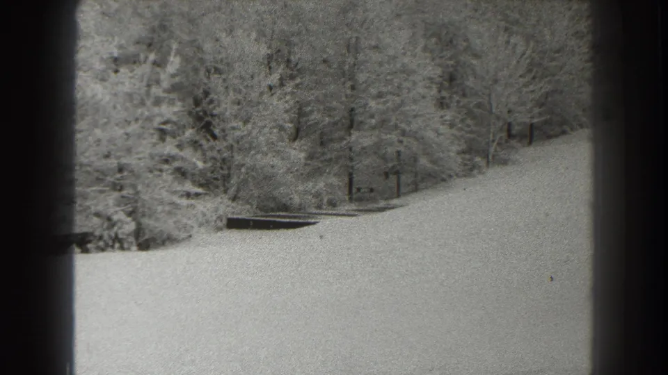 Final 1938 Martinsburg frame holding on a snowy hillside and wooded edge in grainy 8mm monochrome.