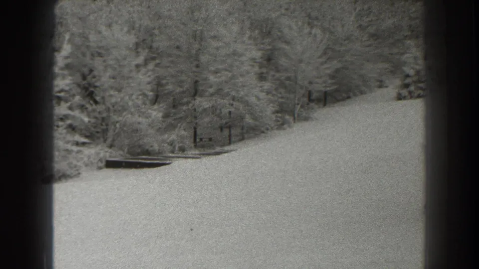 A Martinsburg winter hillside in 1938 home-movie footage, with snow, woods, and a dark edge suggesting filming from a sheltered opening.