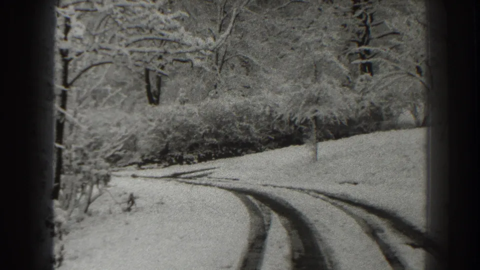 1938 Martinsburg-area home-movie frame showing a quiet snow-covered road with parallel tracks and leafless trees.