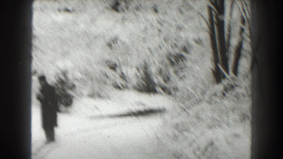 A soft-focus 1938 Martinsburg frame shows a bundled person standing on a snow-covered road in a wooded winter setting.