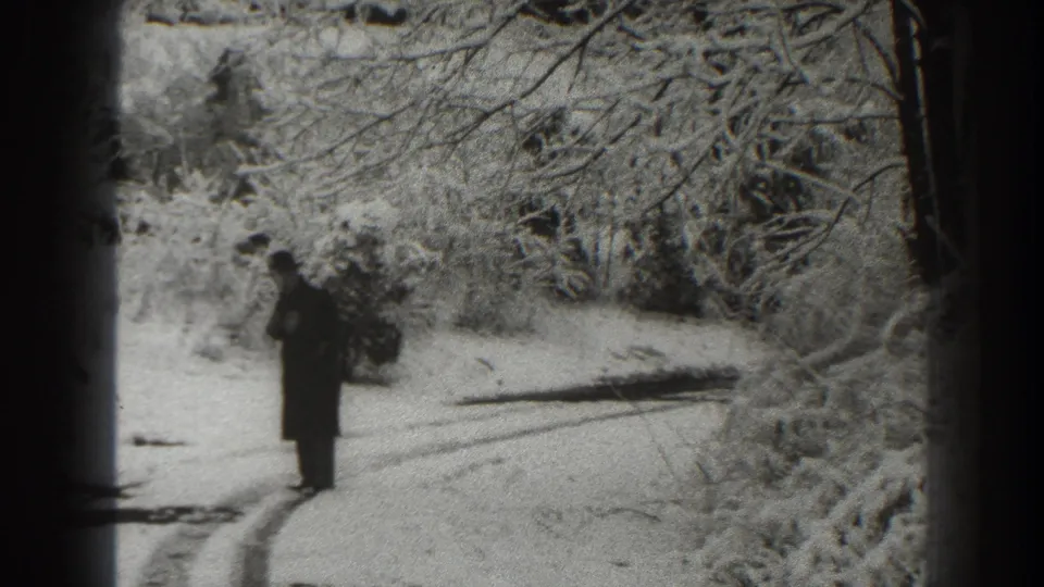 A person in a dark winter coat stands on a snow-covered road in the 1938 Martinsburg home-movie scene.