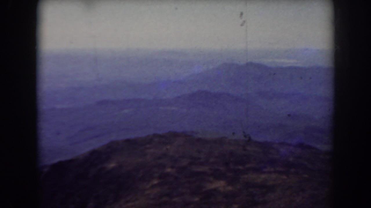 Rocky mountain foreground with hazy ridges and pale sky seen through dark 8mm frame edges.