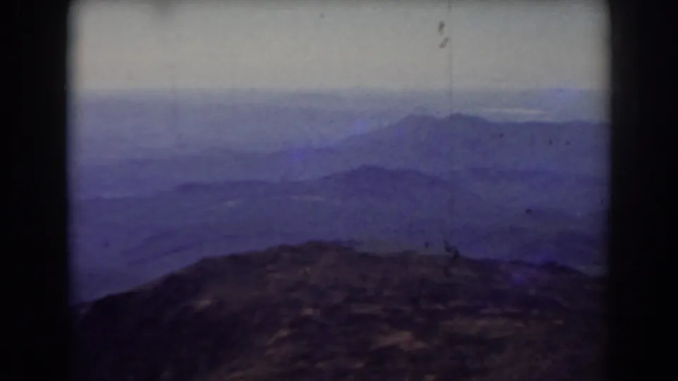1938 Mount Washington home-movie frame showing rocky summit terrain and layered blue-purple mountain ridges under a pale sky.